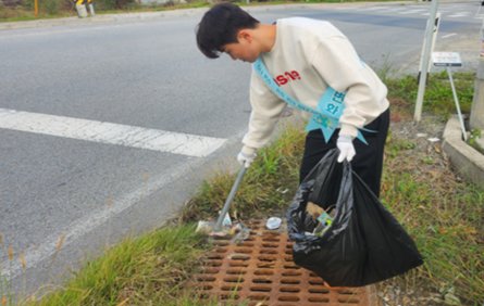 An employee collecting litter near a roadside drain during a riverside cleanup