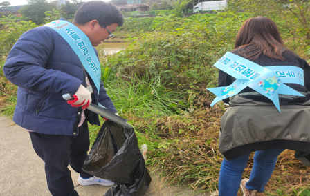 Employees collecting litter from vegetation along a riverside